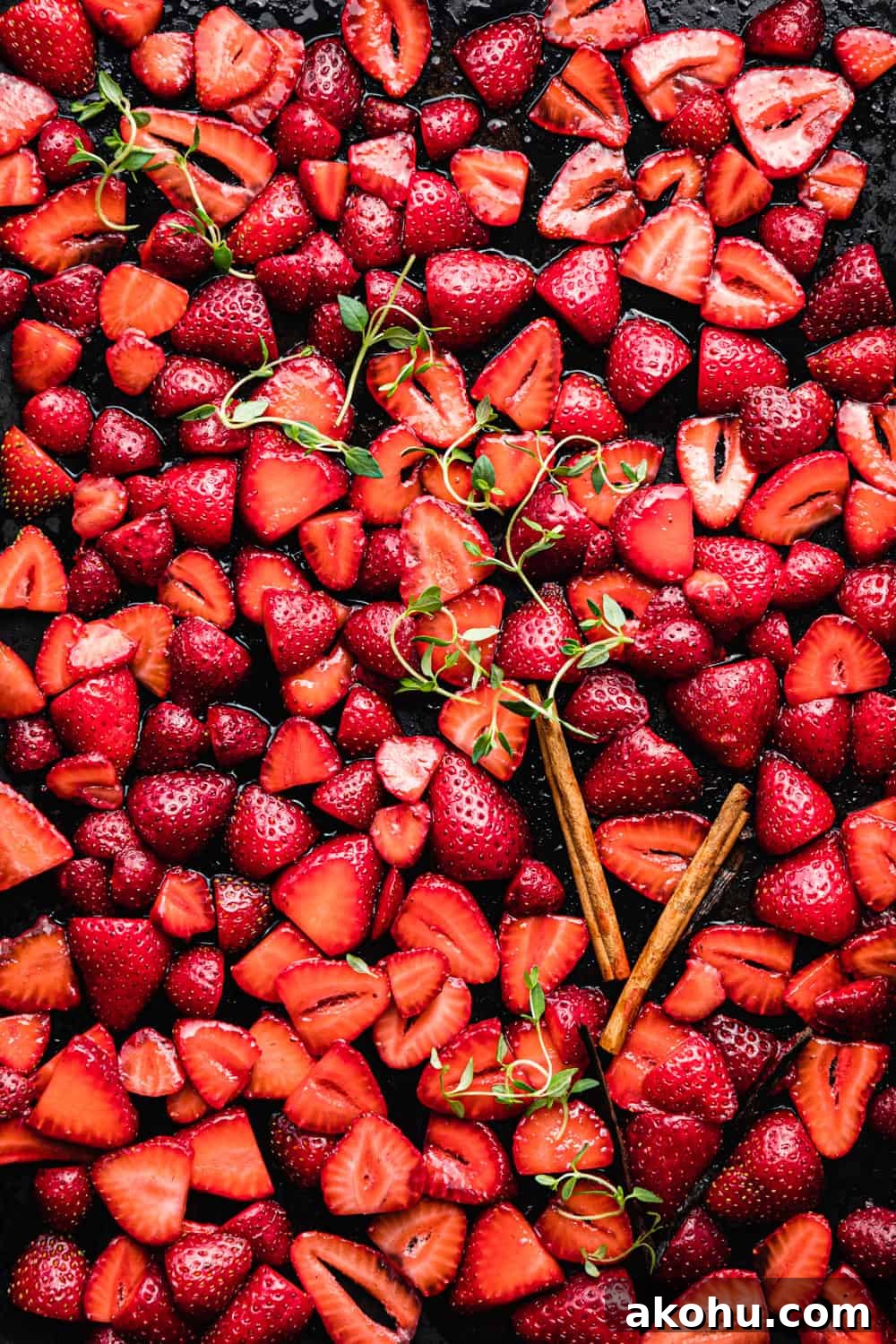 sliced strawberries with sugar, cinnamon sticks, vanilla and thyme on a baking sheet.