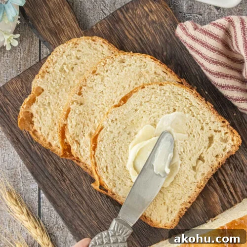 Overhead view of sliced Amish white bread with butter being spread on a slice after baking in a bread machine.