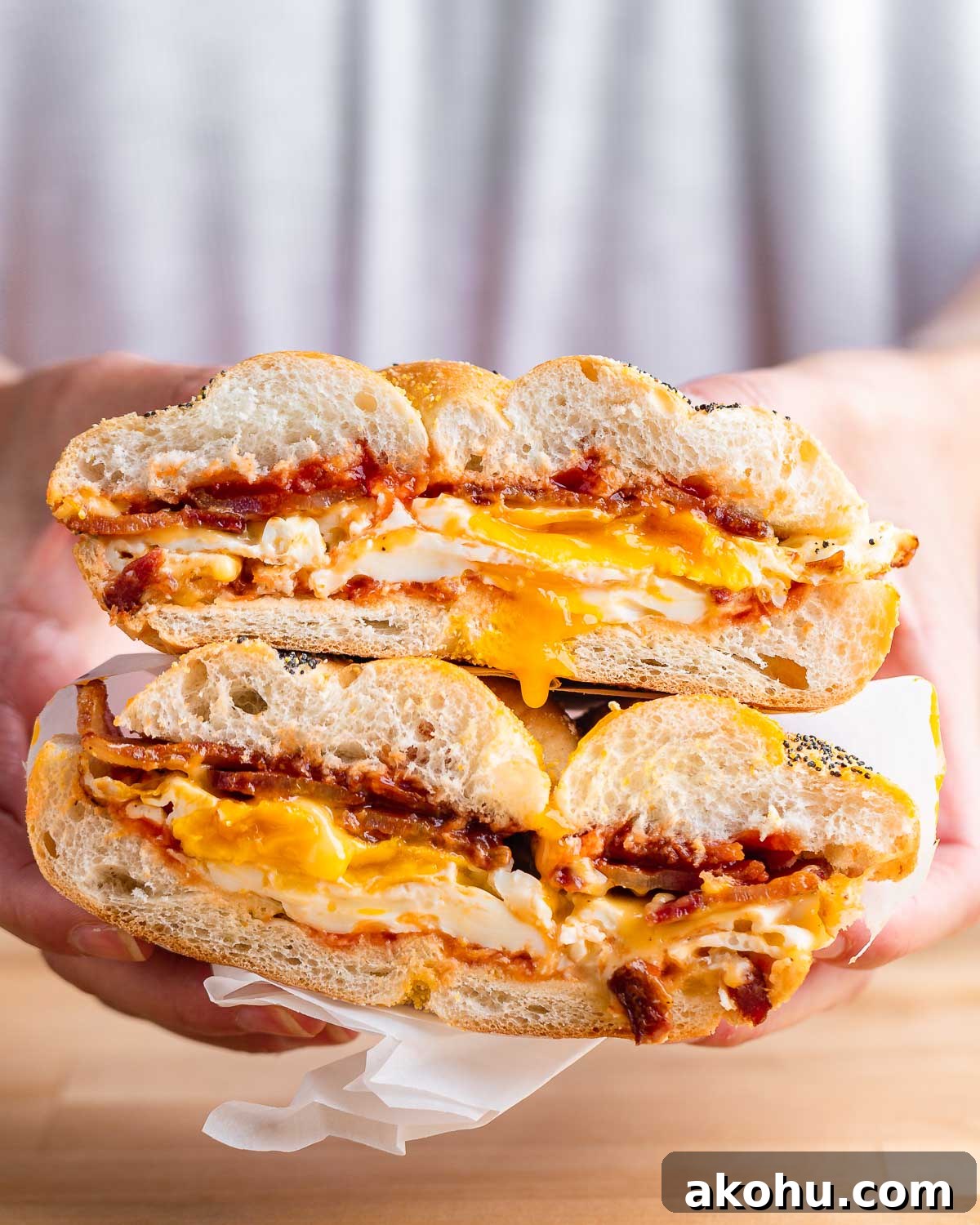 Hands holding a bacon egg and cheese sandwich cut in half with the yolk dripping.