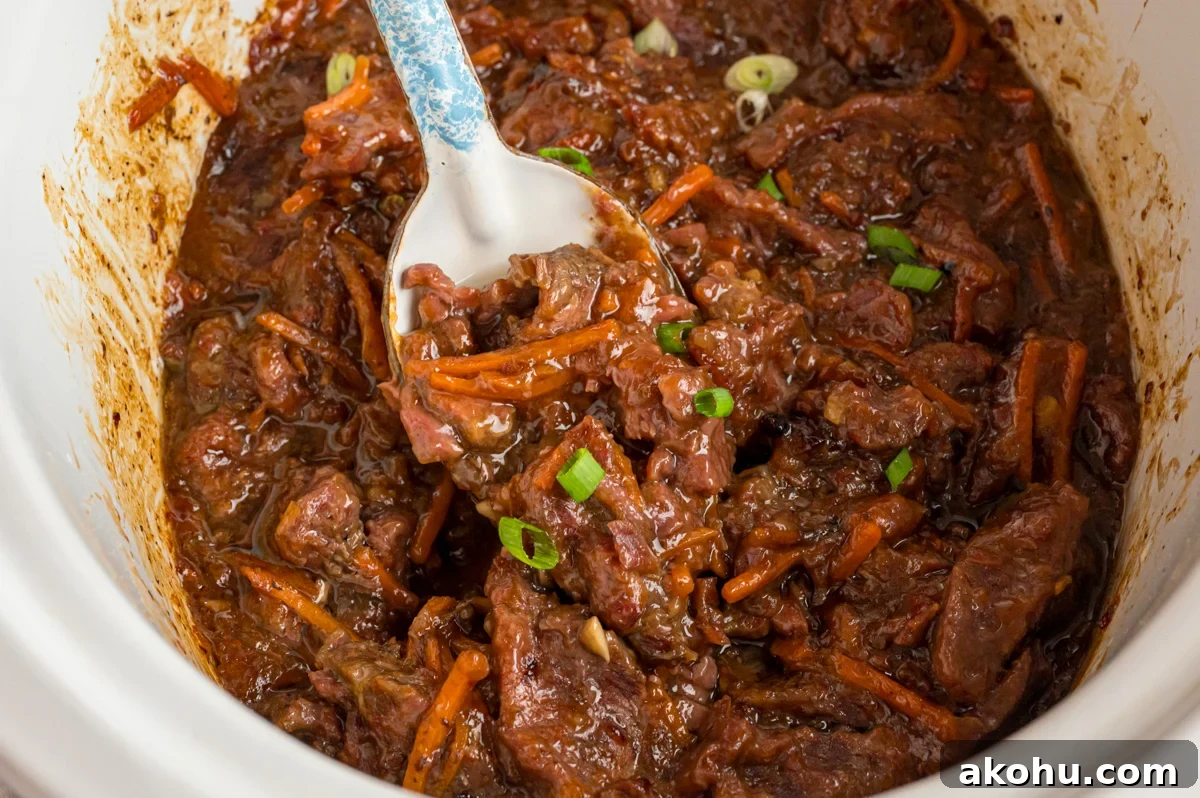 Slow Cooker Mongolian Beef Recipe — Tender Garlic Soy Beef 9 overhead of slow cooker mongolian beef with a spoon scooping some out.