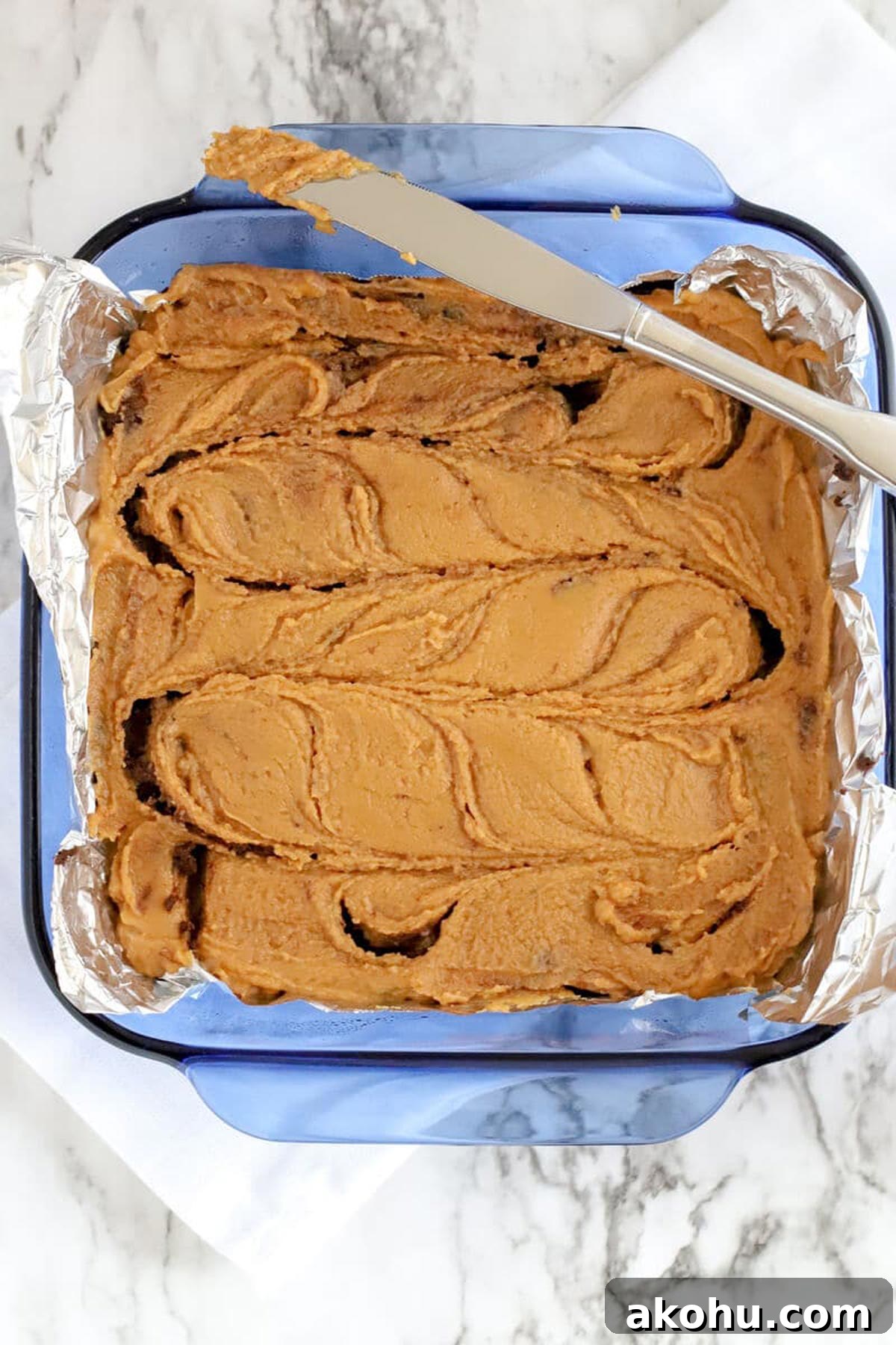 Chocolate Peanut Butter Fudge swirled with a butter knife in a blue baking dish.