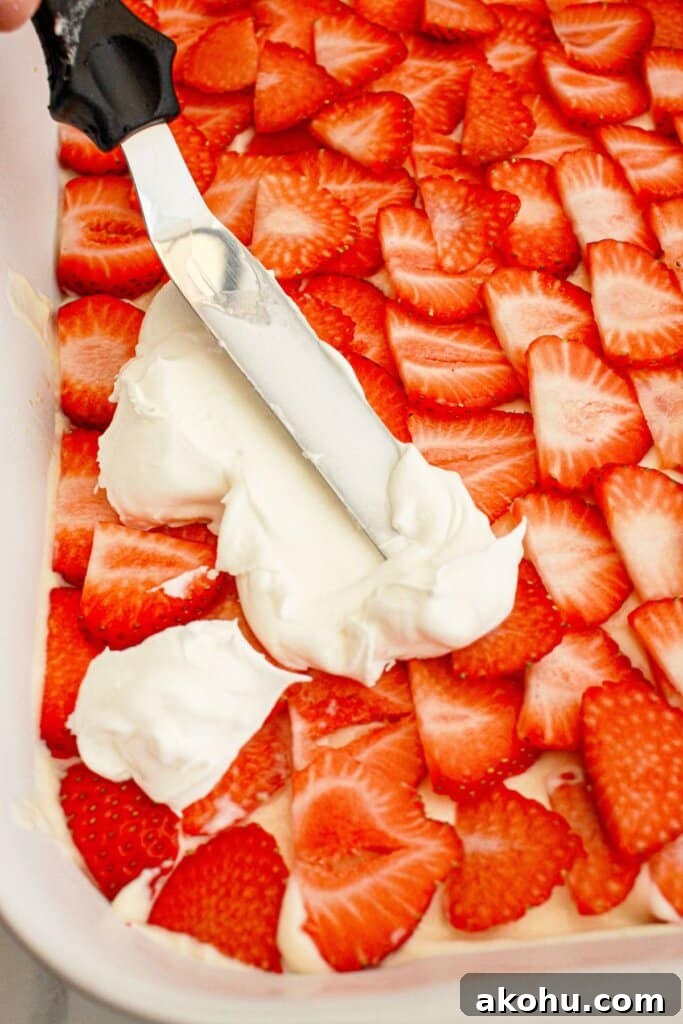 Strawberry Cheesecake Lush Dessert Recipe — No-Bake Layered Treat 9 Cool Whop being spread on top of sliced strawberries.