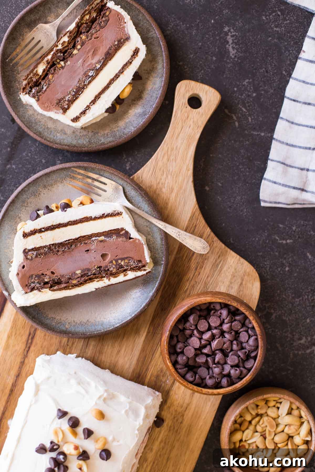 Chocolate Peanut Butter Ice Cream Slice Cake Recipe 3 Two slices of Chocolate Peanut Butter Ice Cream Slice Cake on plates with forks, sitting next to the rest of the cake, along with a bowl of chocolate chips and a bowl of peanuts.
