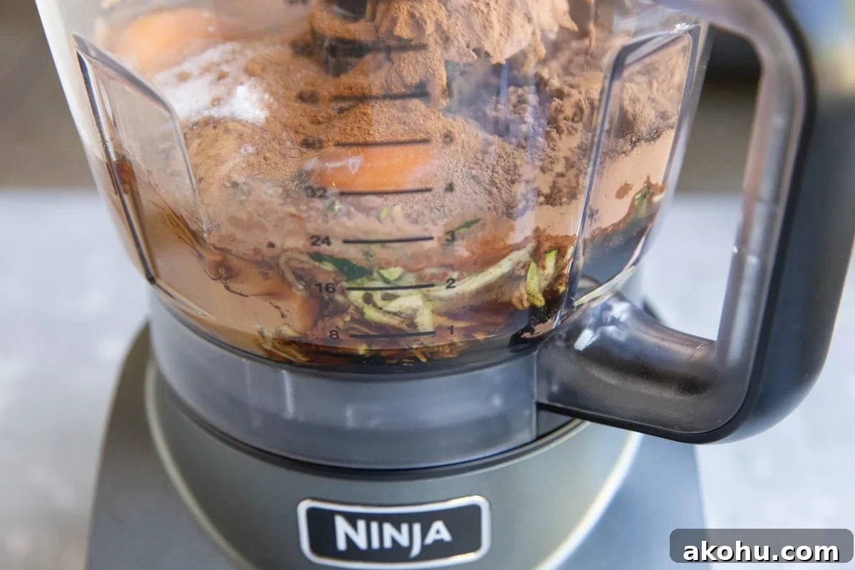 Food processor with ingredients for zucchini chocolate cake.