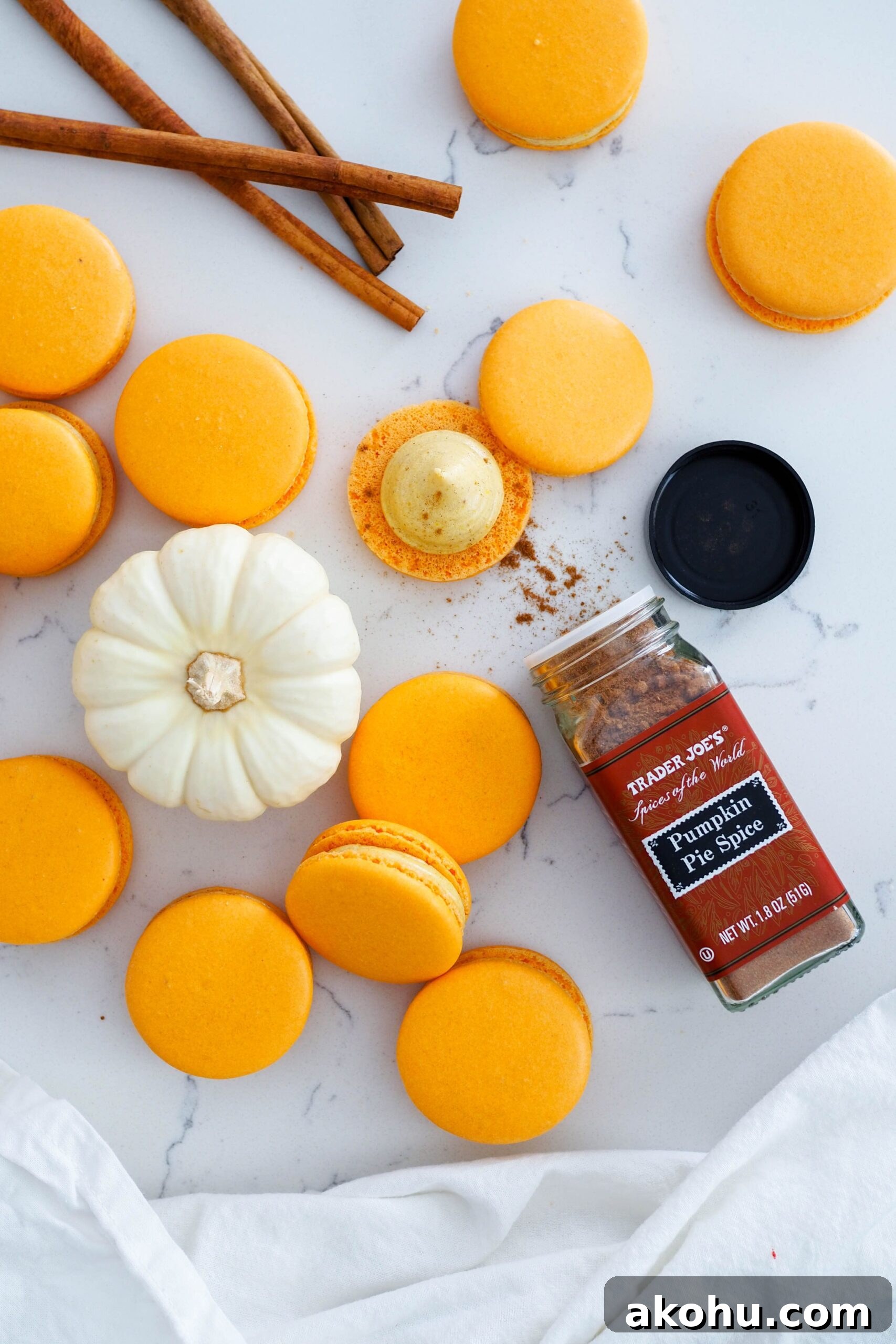 An open jar of pumpkin pie spice next to a stack of macarons and a mini white pumpkin.