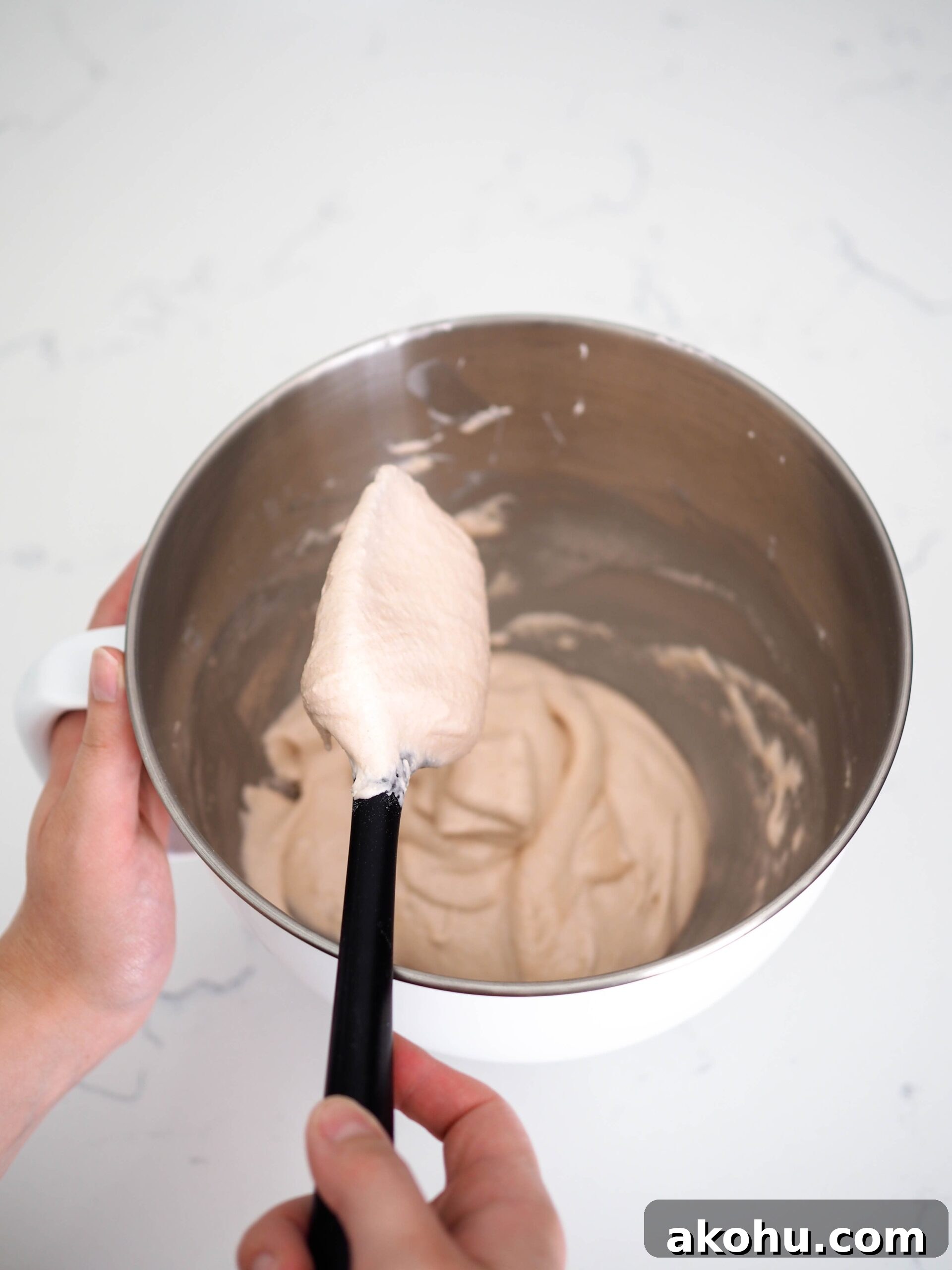 A spatula has macaron batter falling off it in ribbons.