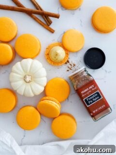 An open jar of pumpkin pie spice next to a stack of macarons and a mini white pumpkin.