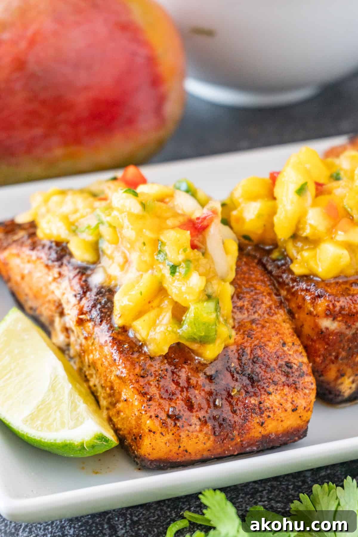 Pan-Seared Salmon with Fresh Mango Salsa 2 Salmon topped with Mango Salsa on a white plate, with lime wedges near the salmon.