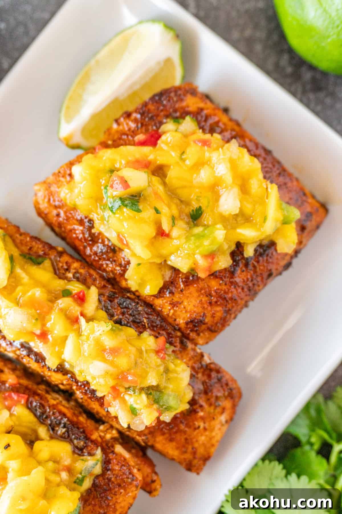 Pan-Seared Salmon with Fresh Mango Salsa 13 Salmon topped with Mango Salsa on white plate, with lime wedges near salmon.