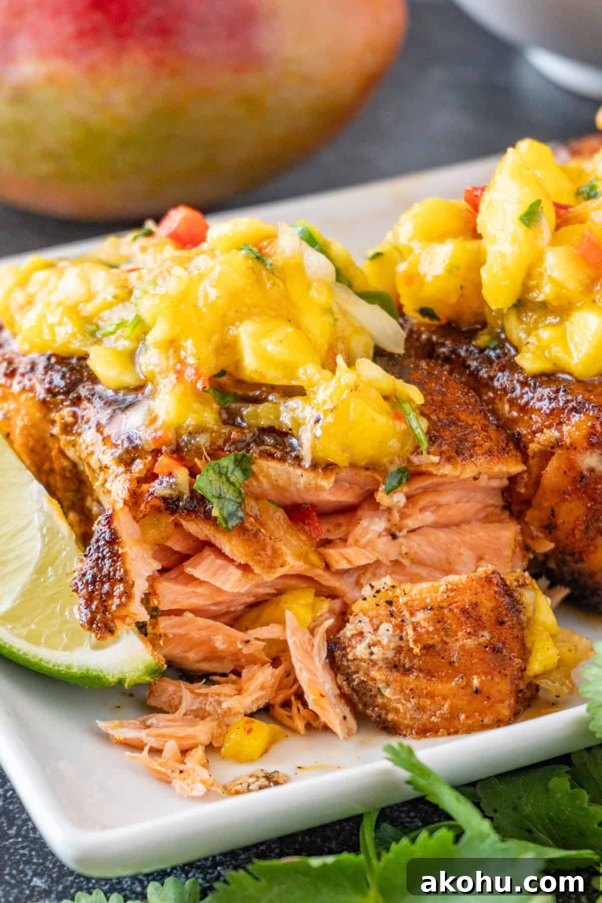 Pan-Seared Salmon with Fresh Mango Salsa 3 Salmon cut open to show cooked flaky layers, topped with mango salsa, sitting on a white plate.