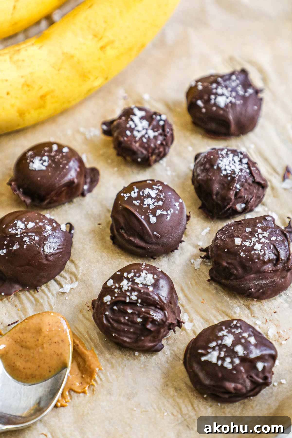 Frozen chocolate-covered banana bites with peanut butter and flaky sea salt on a parchment paper-lined baking sheet.