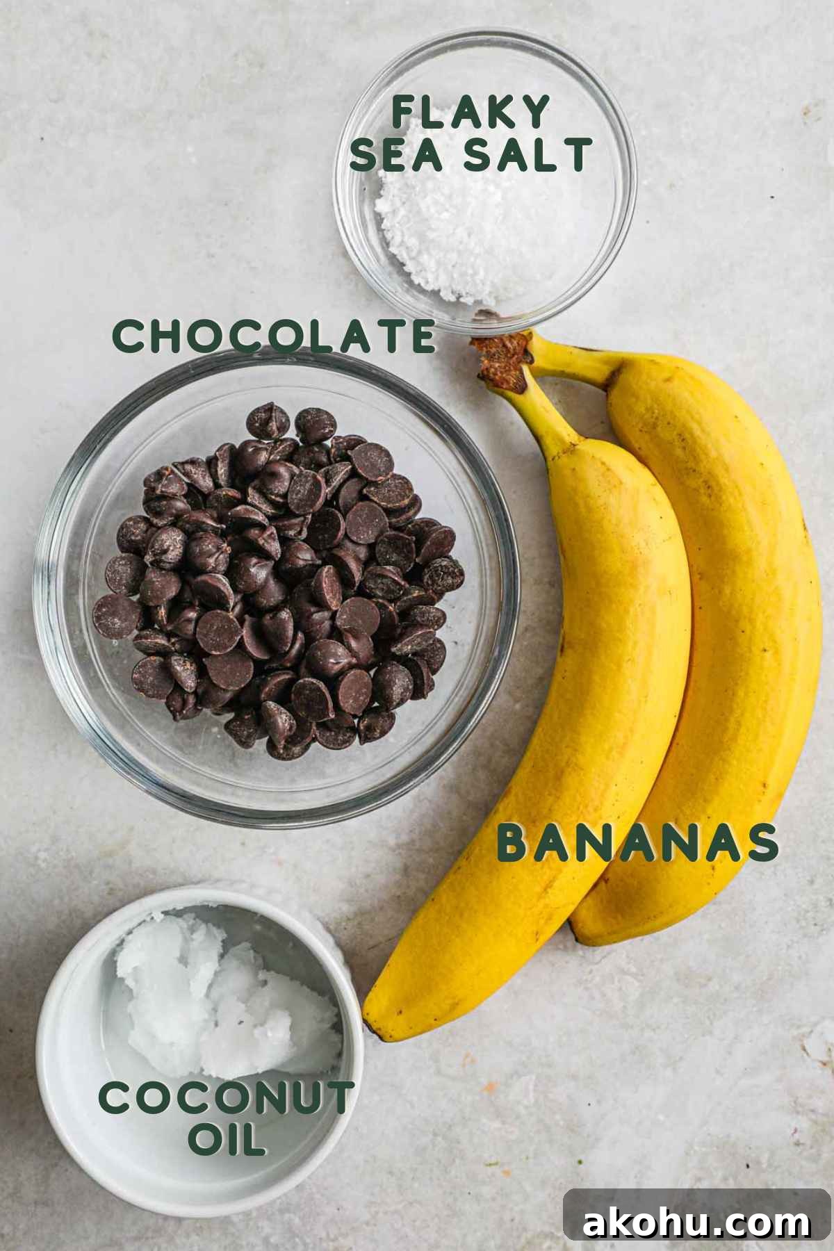 Ingredients to make chocolate-covered bananas, including chocolate, sliced bananas, coconut oil (optional), and flaky sea salt.