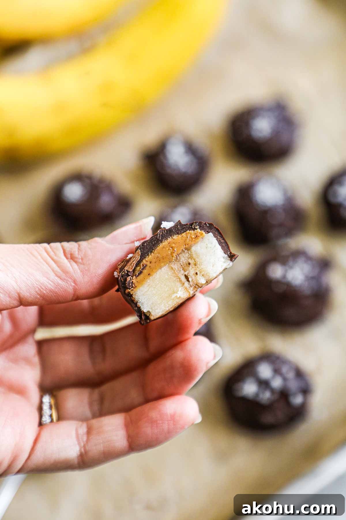Hand holding a frozen chocolate covered banana bite cut in half with chocolate, banana, and peanut butter.