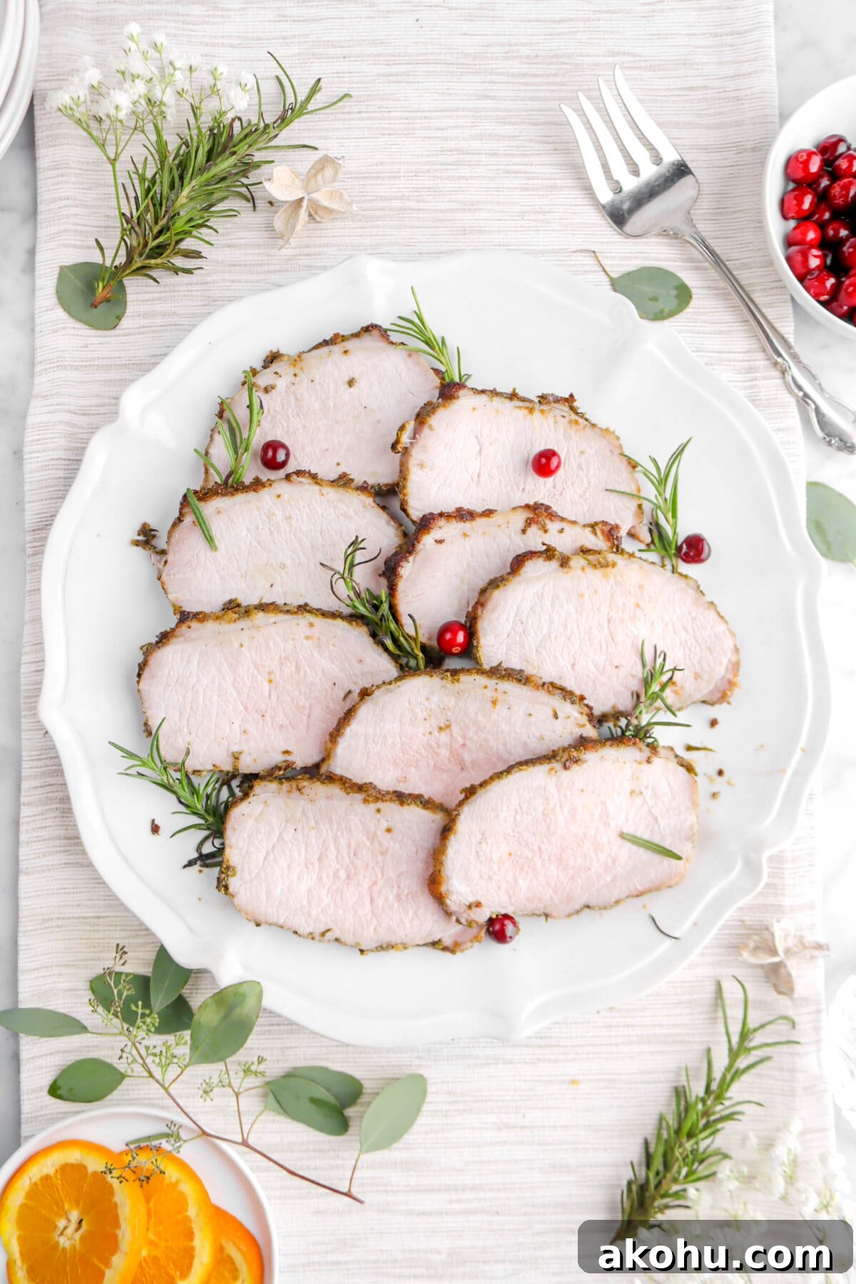 slices of pork tenderloin on around platter with fresh cranberries and rosemary sprigs tucked in, with serving fork and rosemary sprigs around.