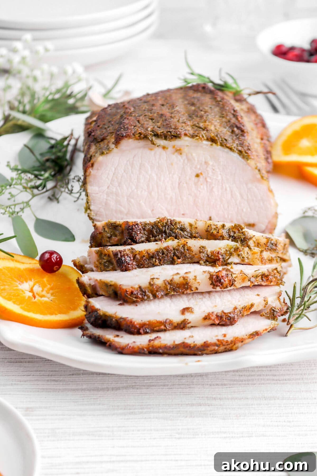 close up of pork tenderloin with five slices laying in front on round platter with rosemary sprigs and orange slices around.