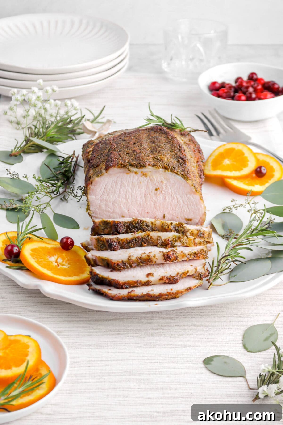 front shot of pork tenderloin slices on white platter with slices and greenery around.
