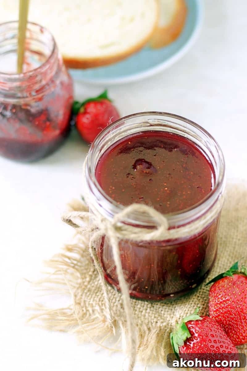 Holiday Instant Pot Strawberry Jam Recipe 11 a small mason jar filled with strawberry jam made in the instant pot in the centre and a white bread ready to be smeared with jam in the background