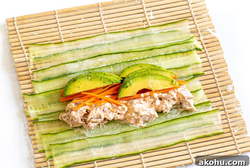 Assembling the cucumber sushi rolls on a sushi mat lined with plastic wrap.