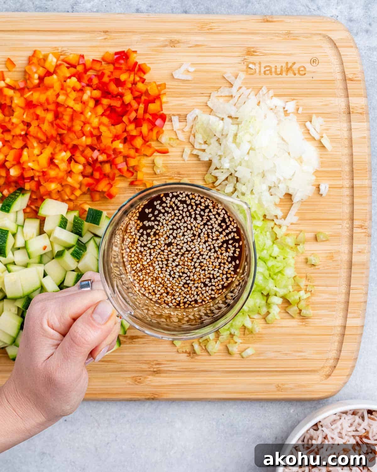 A hand holding a cup of liquid over a cutting board of chopped vegetables.