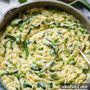 Top down view of creamy orzo pasta with peas and spinach in a pan